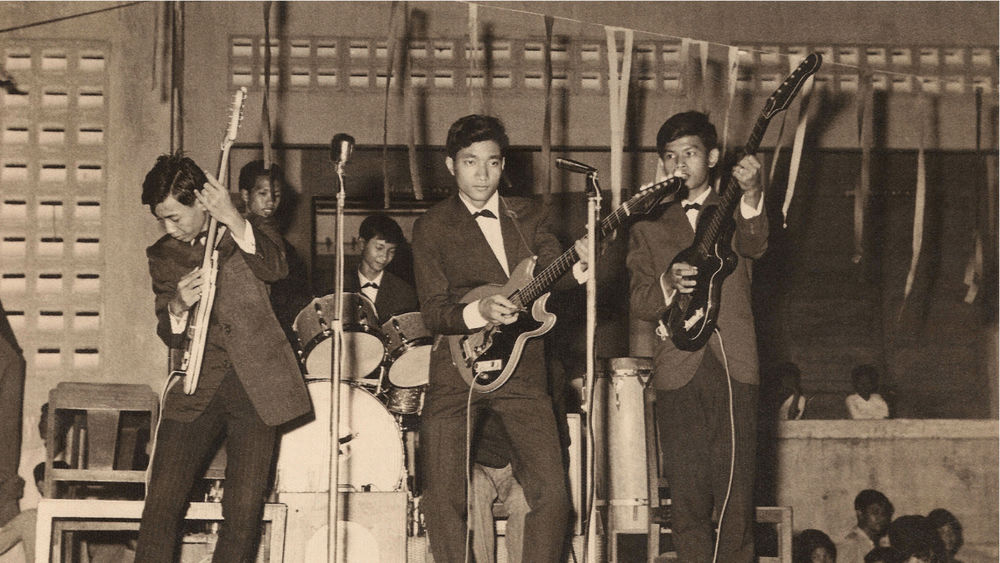 A black and white image of six male and female musicians performing on stage.